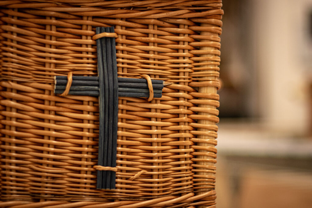 Woven willow coffin with a black woven cross motif.